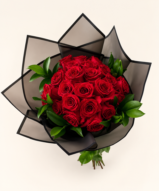 A bouquet of 50 vibrant red roses with green leaves, wrapped in a stylish black and dark gray translucent paper sleeve, shown from a top-down view on a light beige background.